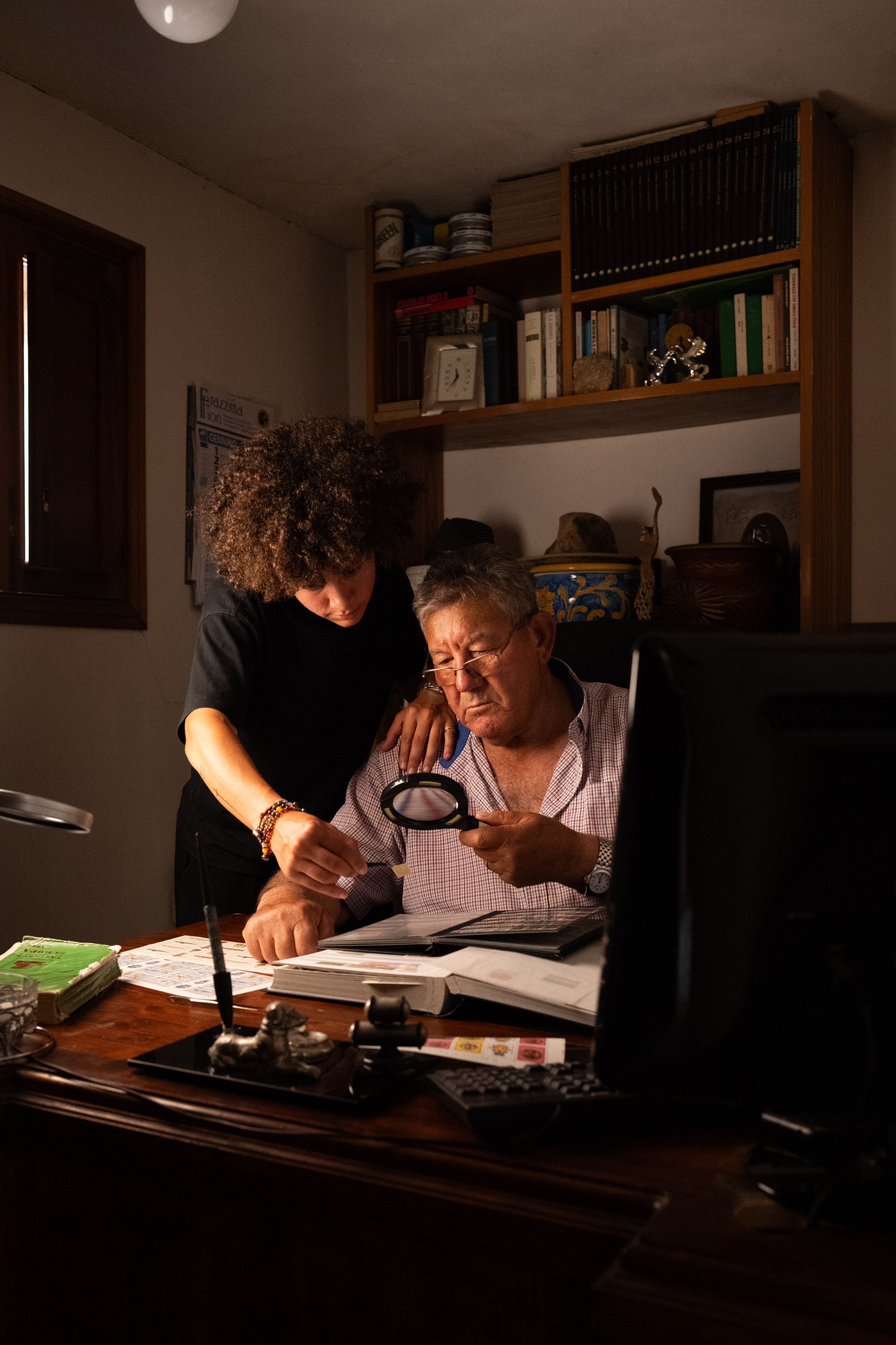 Flavia e il nonno alla scrivania, intenti a esaminare la collezione con lente e pinzette
